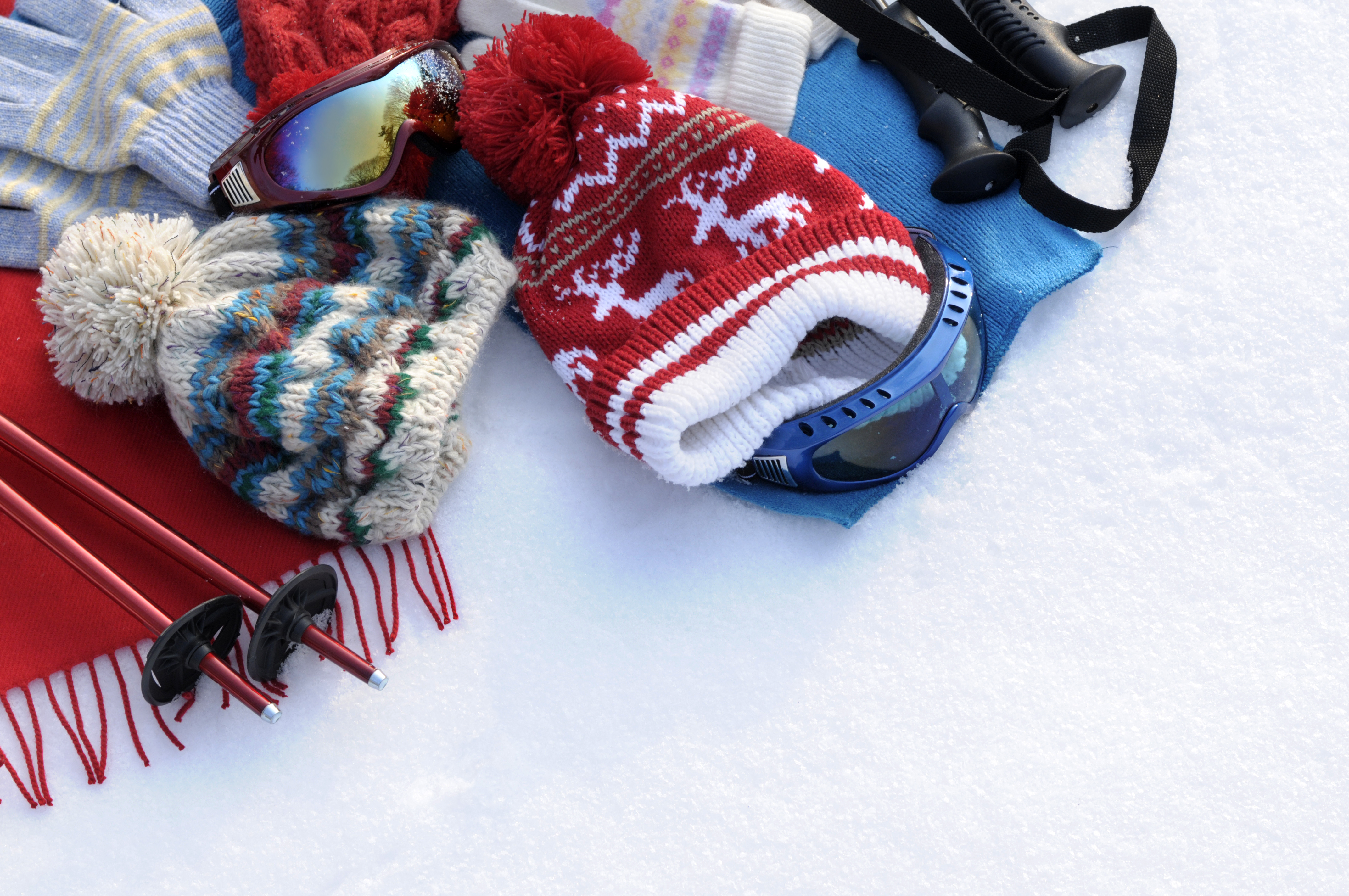 Winter sports background with ski poles, goggles, hats and gloves with copyspace (picture taken in fresh snow with directional winter sun).